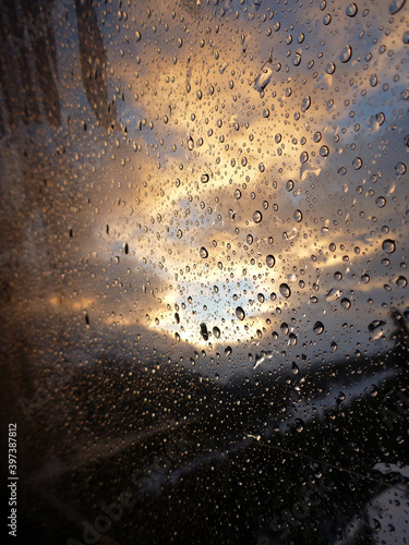 Vertical close-up view of water droplets on a glass window in winter, with snow covered mountains near sunrise outside