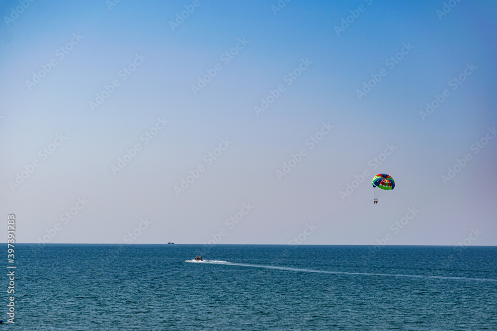 A rainbow-colored striped parachute with two passengers under it. People flying over the blue sea. Entertainment at the resort and active recreation on vacation and on vacation A rainbow-colored striped parachute with two passengers under it. People flying over the blue sea. Entertainment at the resort and active recreation on vacation and on vacation