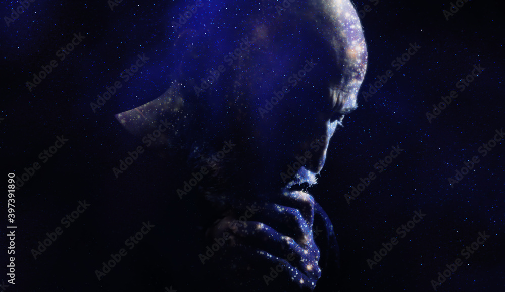 Double exposure of a faithful man praying God with a rosary in his old wrinkled hands, trembling, and a beautiful starscape.
