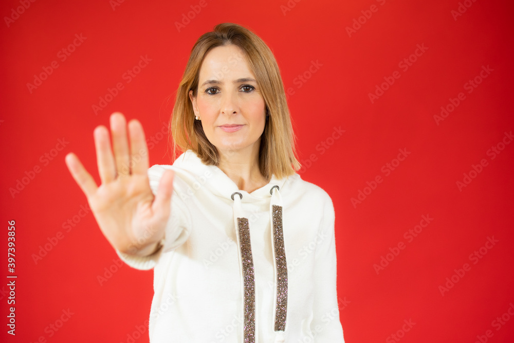 Portrait of a serious young woman standing with outstretched hand showing stop gesture isolated over red background Portrait of a serious young woman standing with outstretched hand showing stop gesture isolated over red background