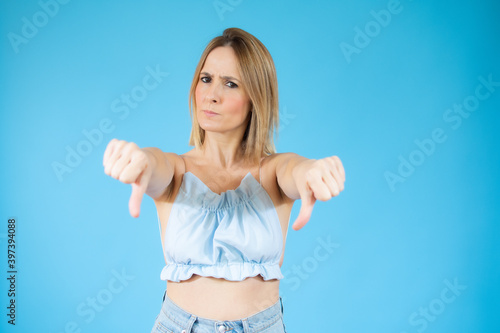 Portrait of displeased woman who is showing thumb down over blue background