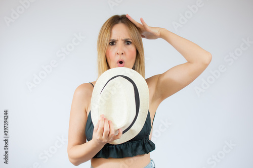 Portrait of young woman holding a straw hat and touching her head and expressing worry isolated over white background
