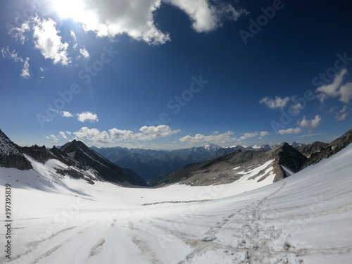 A footprints on the snow, lying on a glacier under Hohe Sonnblick in Austrian Alps. The footprints lead in one direction. Many high mountain chains in the nearby. Clear and sunny day. Mountainerring
