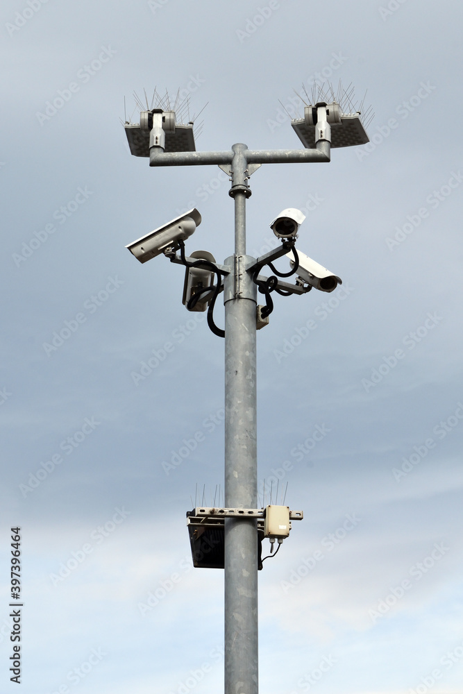Isolated Metal Pole with Lights & CCTV Equipment against Cloudy Sky Isolated Metal Pole with Lights & CCTV Equipment against Cloudy Sky