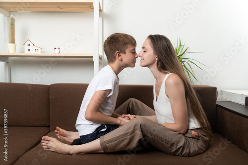 Mom and son rub their noses while sitting on couch at home. Close and friendly family relationships.