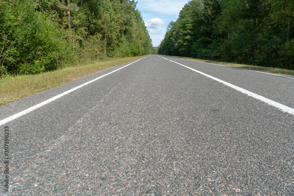 Obraz premium Empty asphalt road through woods and fields. New fresh asphalt pavement away from the city. Development of rural infrastructure. Road marking lines close up.