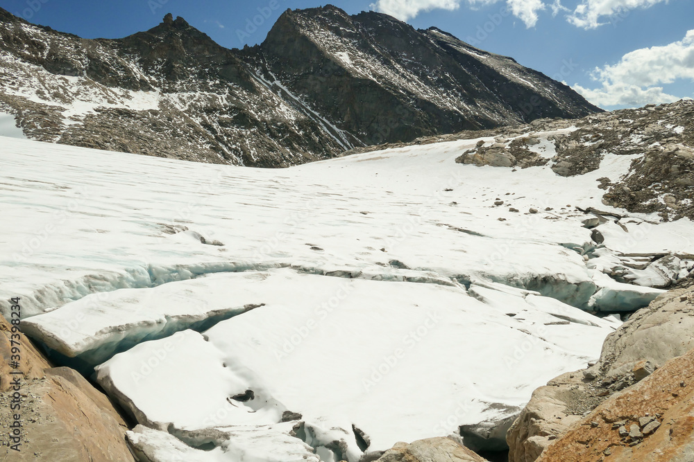 Obraz premium A footprints on the snow, lying on a glacier under Hohe Sonnblick in Austrian Alps. The footprints lead in one direction. Many high mountain peaks. Clear and sunny day. Creeks on the glacier