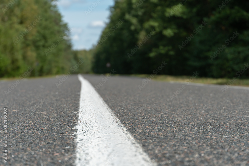 Empty asphalt road through woods and fields. New fresh asphalt pavement away from the city. Development of rural infrastructure. Road marking lines close up.
