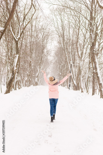 Young girl in a snowy forest in winter. Portrait of a girl in a winter park with running snow. A woman goes catching snowflakes
