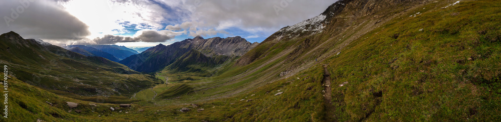 A panoramic view on vast valley with the view on Gro?glockner in Heiligenblut region in Austria. The  valley has lush green color. There are high Alpine chains in the back. A bit of overcast