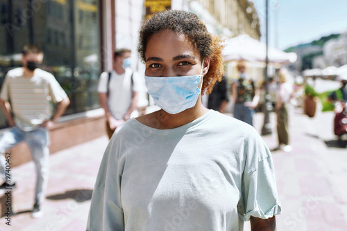 Portrait of young african american woman wearing mask looking at camera. People collecting their orders from the pickup point during coronavirus lockdown in the background