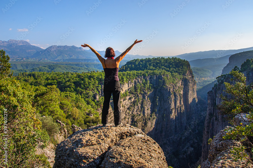 A girl with her arms raised high is standing on the edge of a deep canyon. Turkey