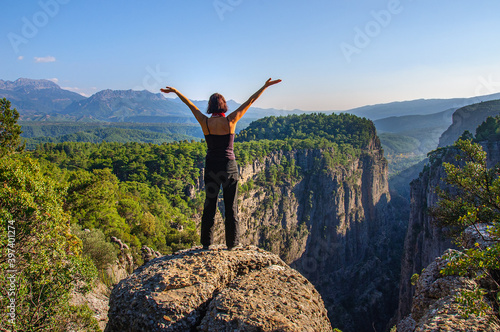 A girl with her arms raised high is standing on the edge of a deep canyon. Turkey