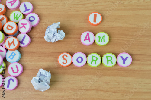 Top view of paper waste, alphabet erasers with text I AM SORRY over wooden background .