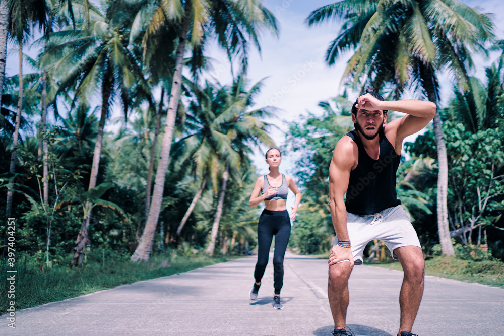 Obraz premium Sport lifestyle. Jogging outdoors. Young couple running under palm trees. Man is tired because of heat.