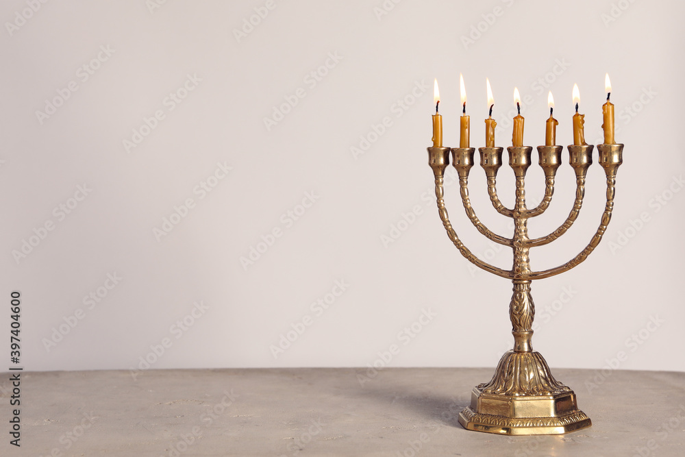 Fototapeta premium Golden menorah with burning candles on table against light grey background, space for text