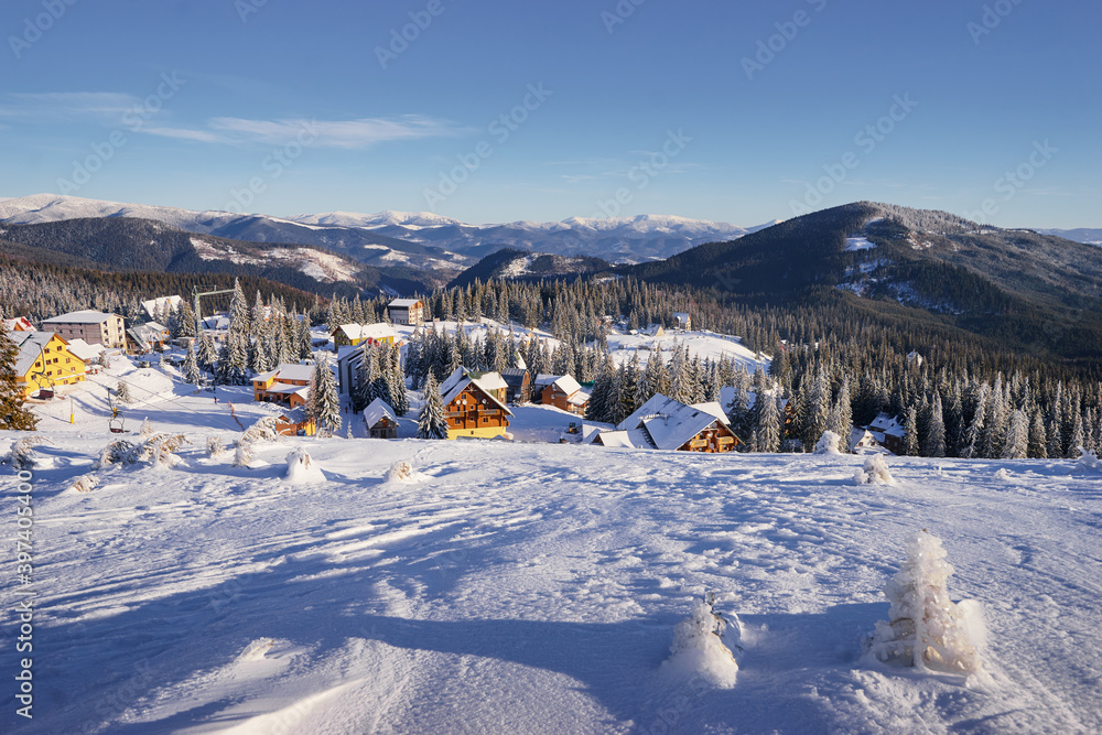 Beautiful white winter wonderland mountain scenery in the Carpathian with traditional houses on a cold sunny day with blue sky.
