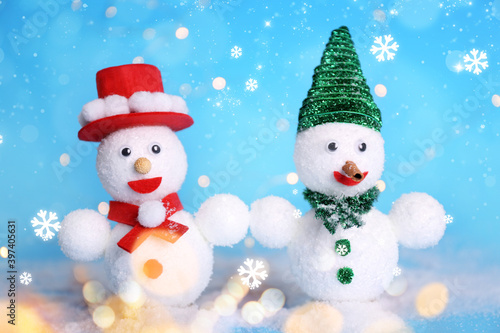 Cute decorative snowmen on light blue background with snowflakes, bokeh effect © New Africa