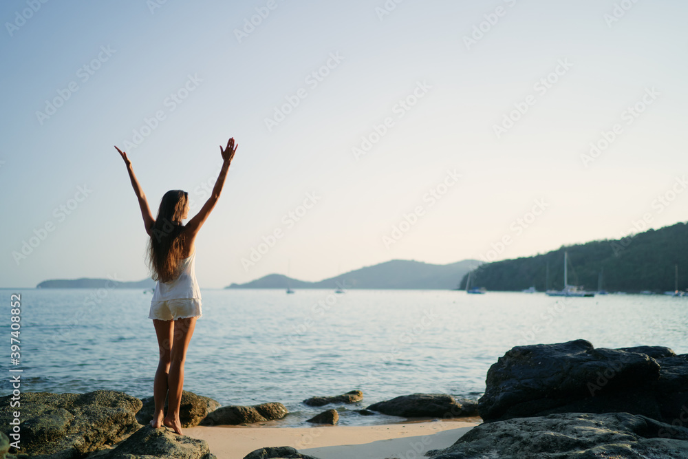 Young woman with long hear standing on sea beach enjoying the view.