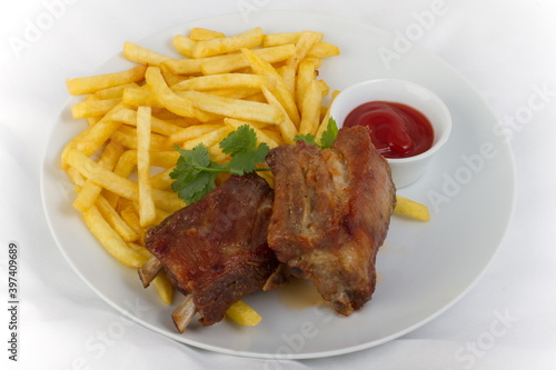 Fried pork ribs with French fries and ketchup on a white plate