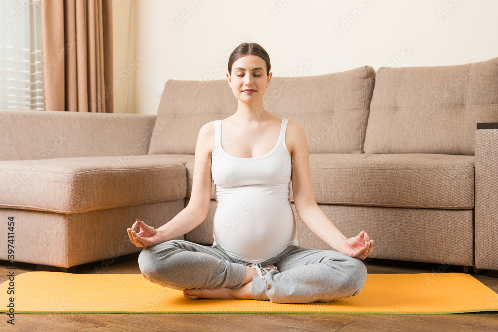 Pregnancy Yoga and Fitness concept at coronavirus time. Pregnant woman meditates indoor in yoga pose. Woman enjoying in meditation