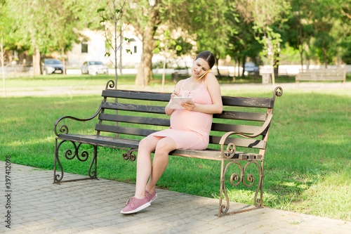 pregnant woman sits on a park bench and writes a to do list to the hospital and talking on the phone