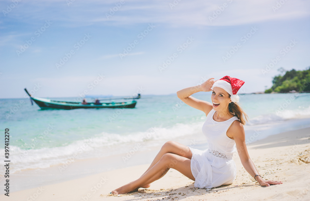 Christmas holidays on tropical sea shore. Young woman in santa claus hat sitting on the beach. Christmas holidays on tropical sea shore. Young woman in santa claus hat sitting on the beach.