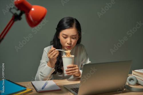 Billede på lærred Asia freelance smart business women eating instant noodles while working on lapt