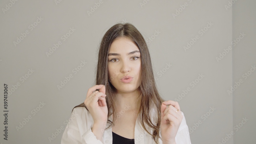 An adult girl in a white medical robe is actively gesticulating during a conversation. Cute brunette with smooth healthy skin and long straight hair. Portrait of a young woman looking into camera. An adult girl in a white medical robe is actively gesticulating during a conversation. Cute brunette with smooth healthy skin and long straight hair. Portrait of a young woman looking into camera.