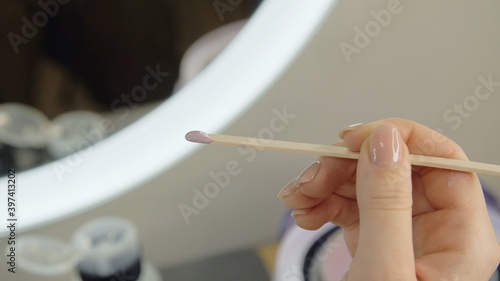 Female well-groomed hand with a beautiful manicure holds a hot wax stick for eyebrow shaping. Wax correction of the shape of the eyebrows with spatula. Beauty industry. Close up. 