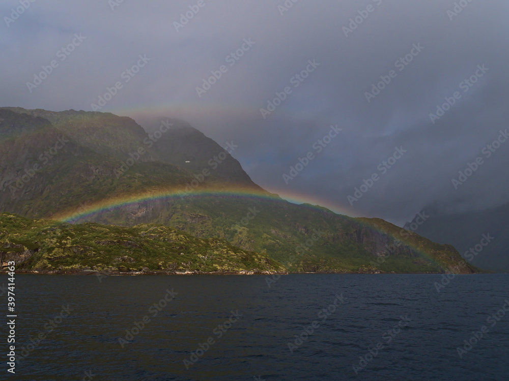 Stunning view colorful double rainbow on the coast of Austvågøya island, Lofoten, Norway on Raftsundet strait with rugged mountains covered by green vegetation on cloudy summer day.