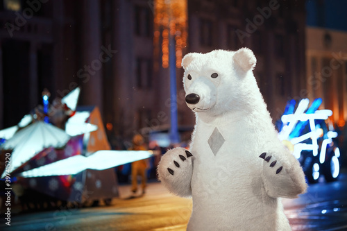 Animator in costume of huge white polar bear walking at night during New Year festival, giant white bear puppet at city street, Christmas outdoors party. Animators dressed as huge puppet of polar bear