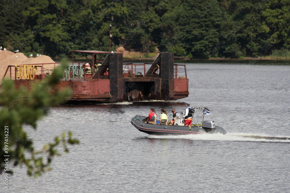 Obraz premium People in life jackets are floating fast on a RIB PVC inflatable motor boat with 90hp powerful outboard motor before a big barge ship bow at summer day, safety of boats drive on water