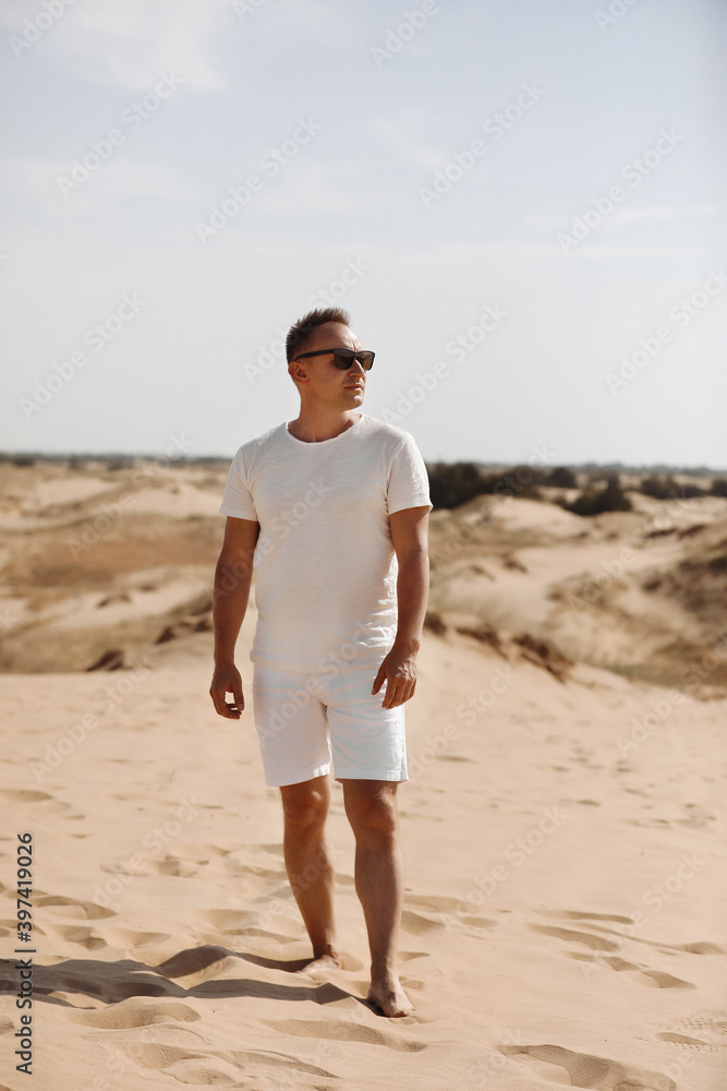 Young handsome man in light clothing and sunglasses in the desert. Concept of freedom relaxation. Place for text or advertising