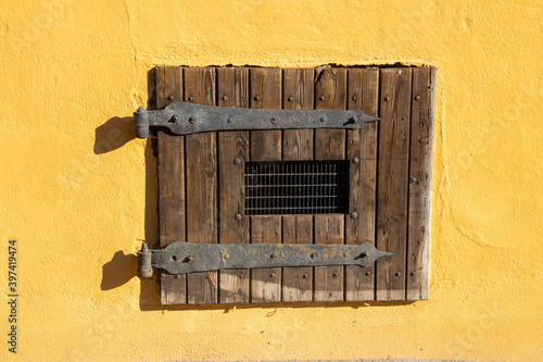 Old vintage wooden shutter with metal grid on a yellow wall
