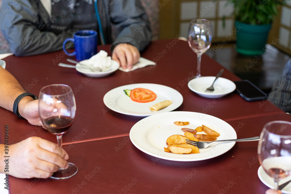 Fototapeta premium wineglass, potato wedges, spring rolls on a dark-red table at end of a party.