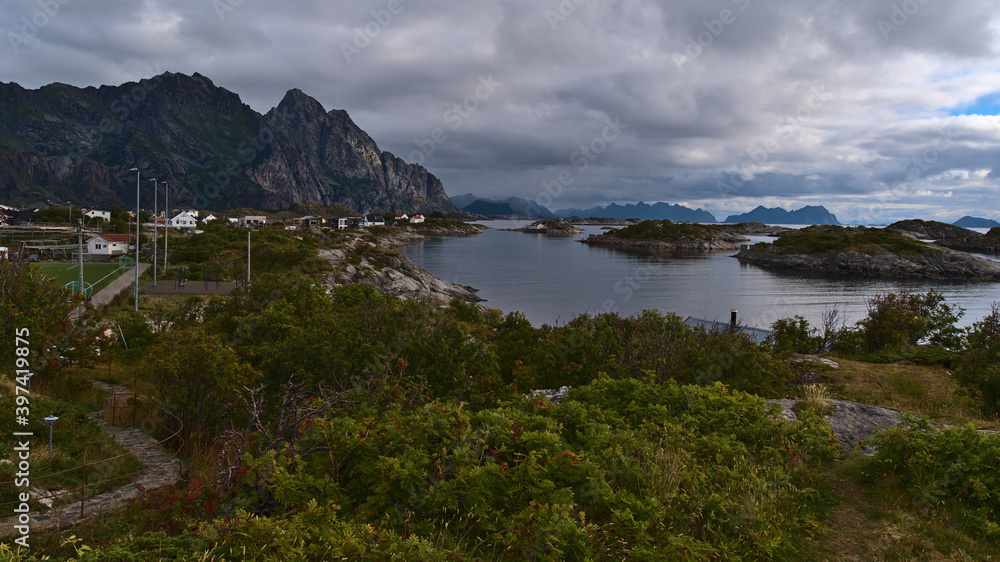 Beautiful view of the rugged mountains on the coast of Austvågøya island, Lofoten, Norway with fishing village Henningsvær, soccer field, houses and rocky islands on cloudy summer day.