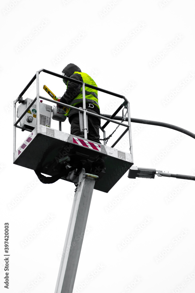 a repairman in overalls on a tower repairing a road lamp. Electrical repair man at work fixing a street light. a repairman in overalls on a tower repairing a road lamp. Electrical repair man at work fixing a street light.