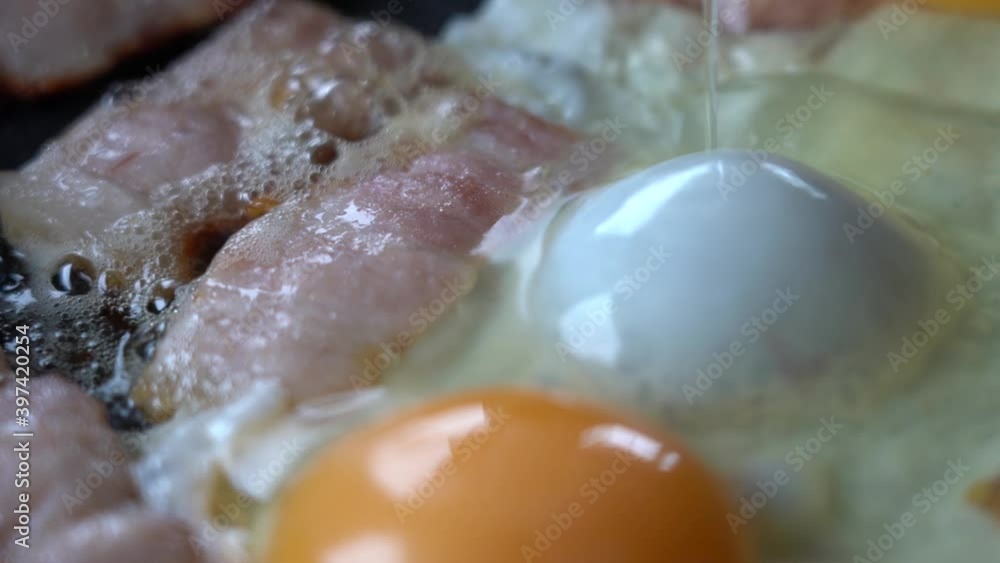 Real life. BACON and EGG are COOKED in a frying pan. Pieces of bacon and eggs in a hot frying pan, close-up. Natural Lighting from the window. Real life. BACON and EGG are COOKED in a frying pan. Pieces of bacon and eggs in a hot frying pan, close-up. Natural Lighting from the window.