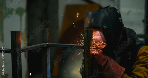 Welder in mask and gloves using semi-automatic electric welding while working with metal construction 