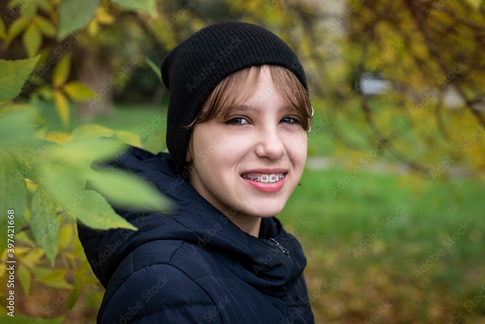 A young teen girl walks in the park and enjoys the cool autumn air, she is wearing a warm jacket and hat, the girl is smiling, she has braces on her teeth A young teen girl walks in the park and enjoys the cool autumn air, she is wearing a warm jacket and hat, the girl is smiling, she has braces on her teeth