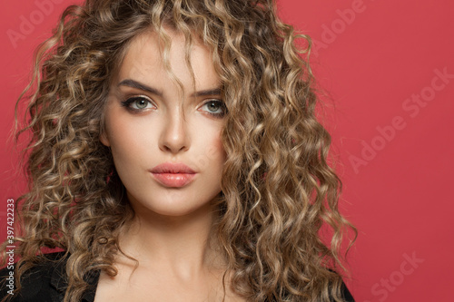 Beautiful woman with curly hair looking at camera on red background