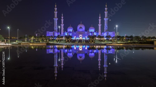 Sheikh Zayed Grand Mosque illuminated at night timelapse, Abu Dhabi, UAE. Evening view from Wahat Al Karama with reflections on water. The 3rd largest mosque in the world photo