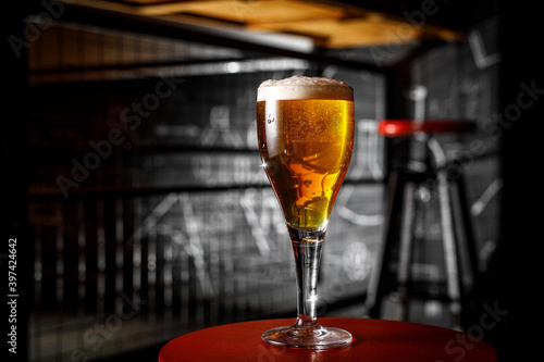 A glass of blond beer on a thin leg in a bar.