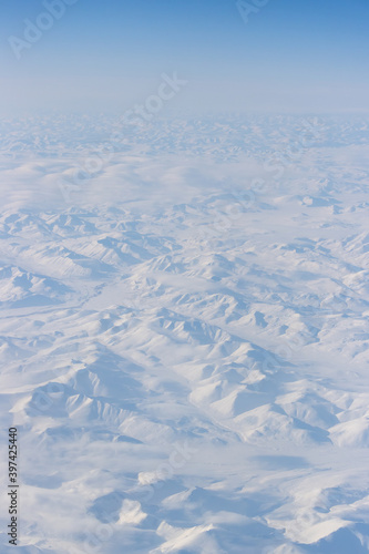 Aerial view of snow-capped mountains and clouds. Winter snowy mountain landscape. Travel to the far north of Russia. Kolyma Mountains, Magadan Region, Siberia, Russian Far East. Beautiful background.