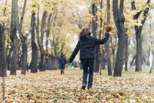 teen girl and boy running through the park and enjoys autumn, beautiful nature with yellow leaves