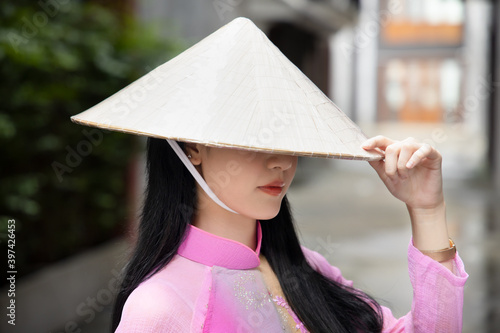 Random anonymous Vietnamese woman in southeast asian travel scene, portrait of exotic asian Vietnam woman in traditional Vietnamese Ao Dai dress with Vietnamese stylized hat photo