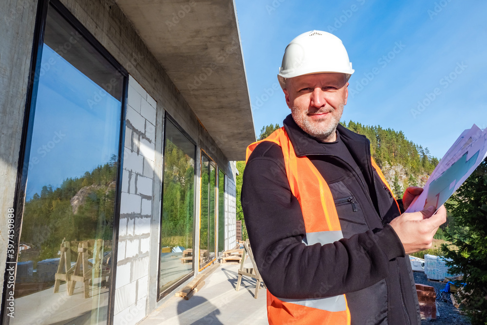 Construction of country houses. A Builder with drawings in his hands smiles at the camera. High-quality construction work. Guarantee of compliance with the terms of construction. Construction of country houses. A Builder with drawings in his hands smiles at the camera. High-quality construction work. Guarantee of compliance with the terms of construction.