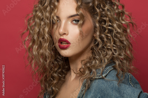 Sensual woman with curly hair on red background, beautiful face close up