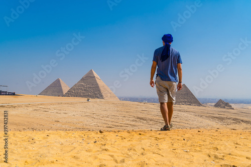 A young man in a blue turban walking next to the Pyramids of Giza, the oldest Funerary monument in the world. In the city of Cairo, Egypt